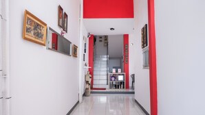 A hallway with a red accent wall, a mannequin, and a shelf with various items. - OYO 2919 Andung Residence (Bandar Lampung)