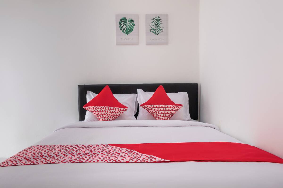 A bed with a white and red bedspread, two red pillows with white text, and two framed botanical prints on the wall.