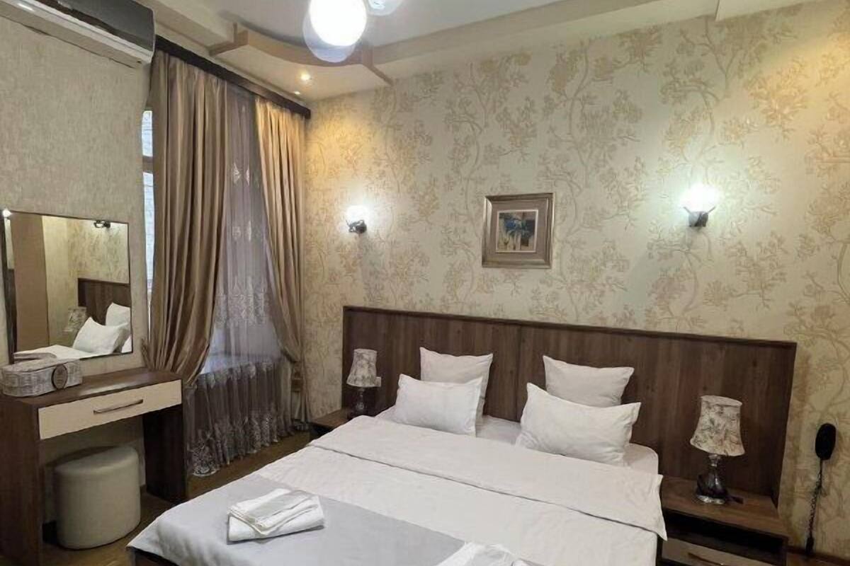 A neatly arranged bedroom with a large bed, bedside tables, a mirror, and a ceiling light fixture.