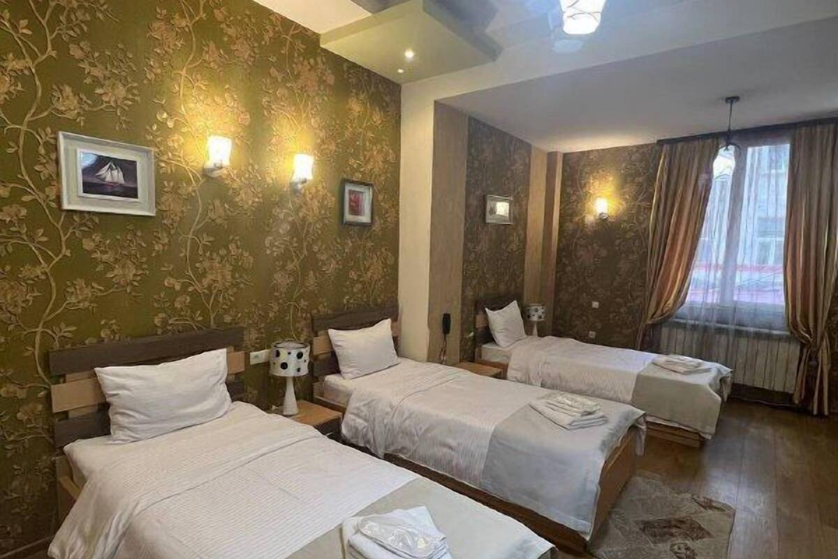 A hotel room with three beds, wooden flooring, and floral wallpaper.