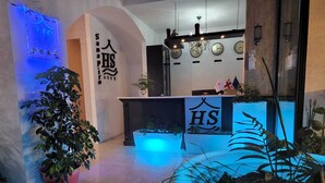 A hotel reception area with a modern design, featuring a reception desk, potted plants, and decorative elements like clocks and flags. - SANAPIRO (Tbilisi)