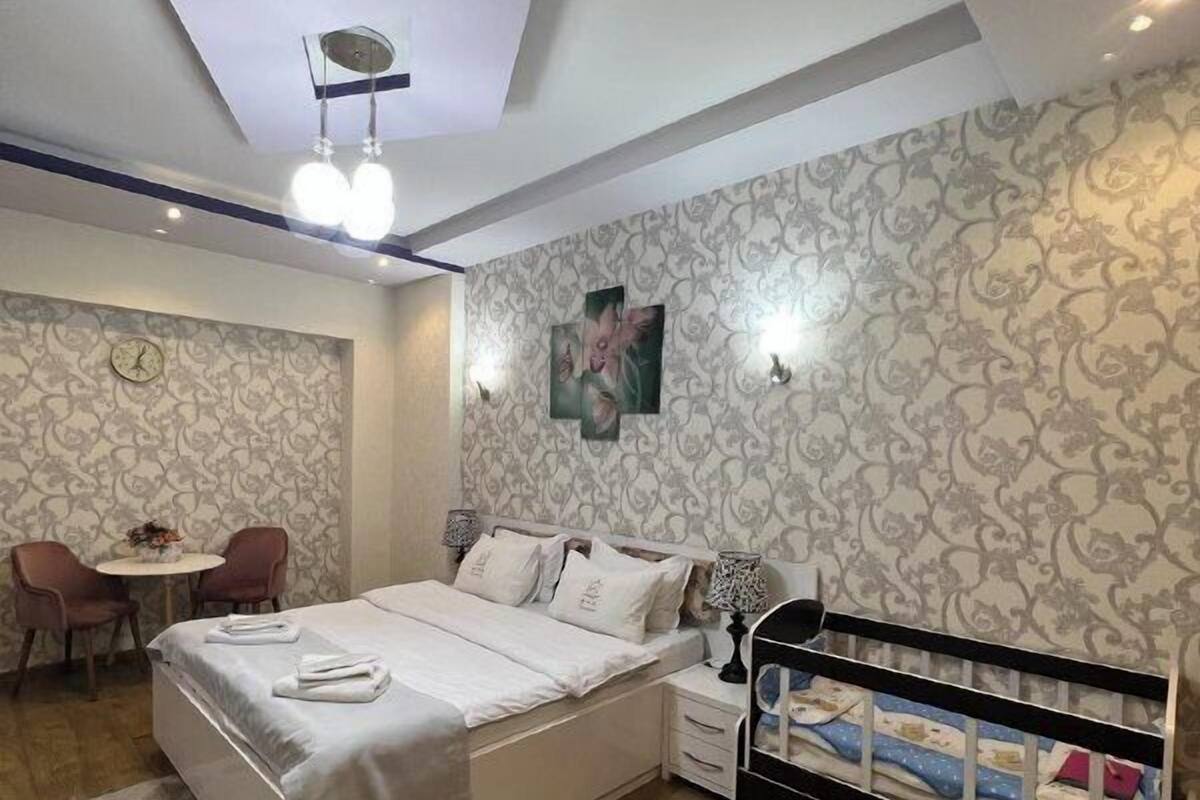 A bedroom with a bed, bedside table, lamp, and a crib.