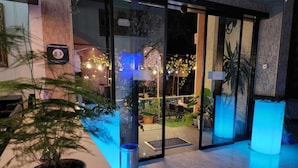 A hotel entrance with glass doors, potted plants, and a sign indicating room rates. - SANAPIRO (Tbilisi)
