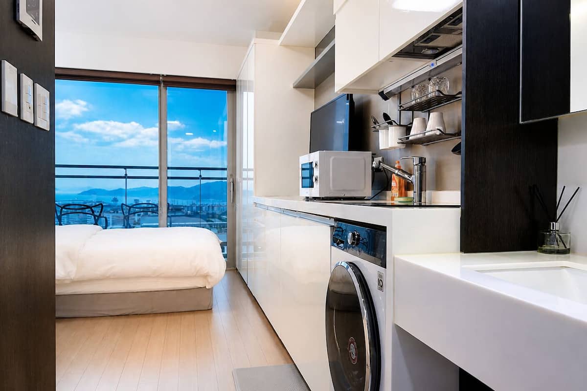 Una habitación de hotel compacta con cama, lavadora, microondas y lavamanos.