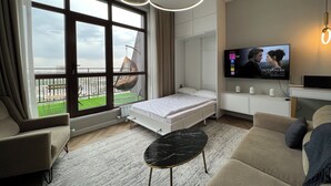 Una habitación de hotel moderna con un ventanal grande, una silla colgante, una cama, un televisor y una mesita.