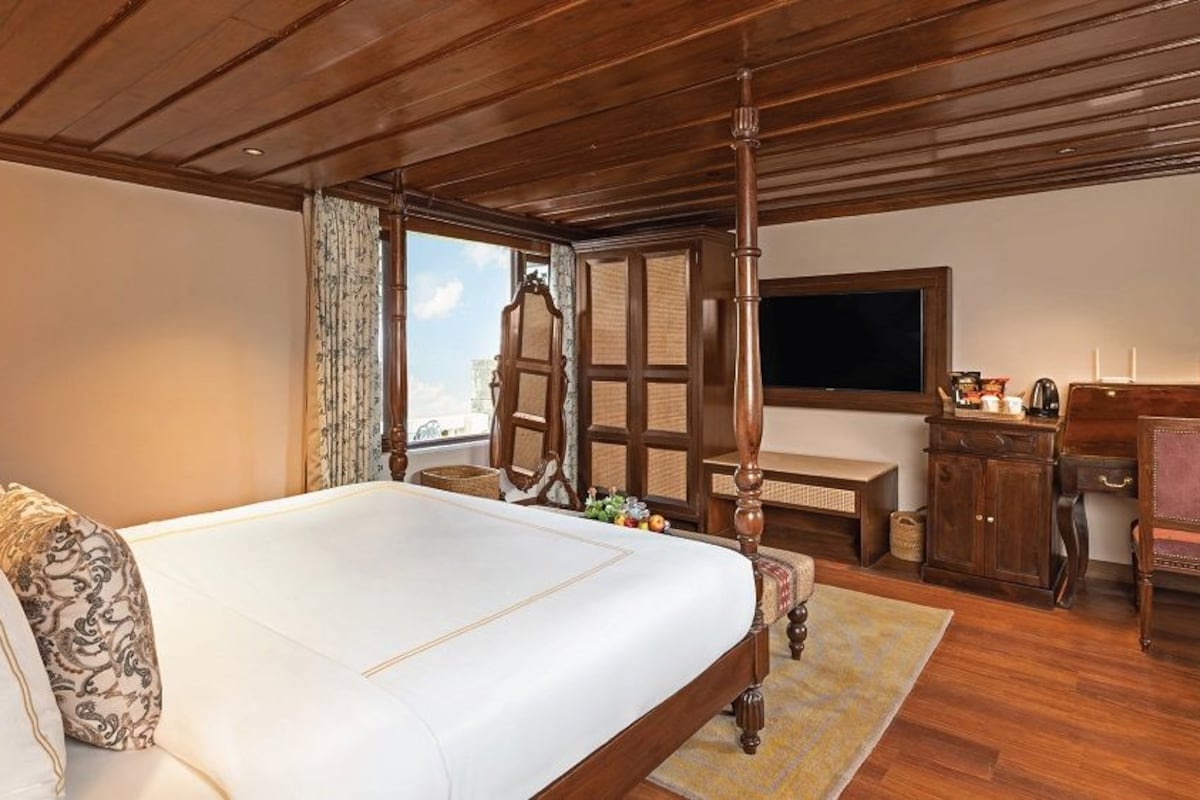 A bedroom with a large bed, wooden ceiling, a desk with a chair, a television, and a window with curtains.