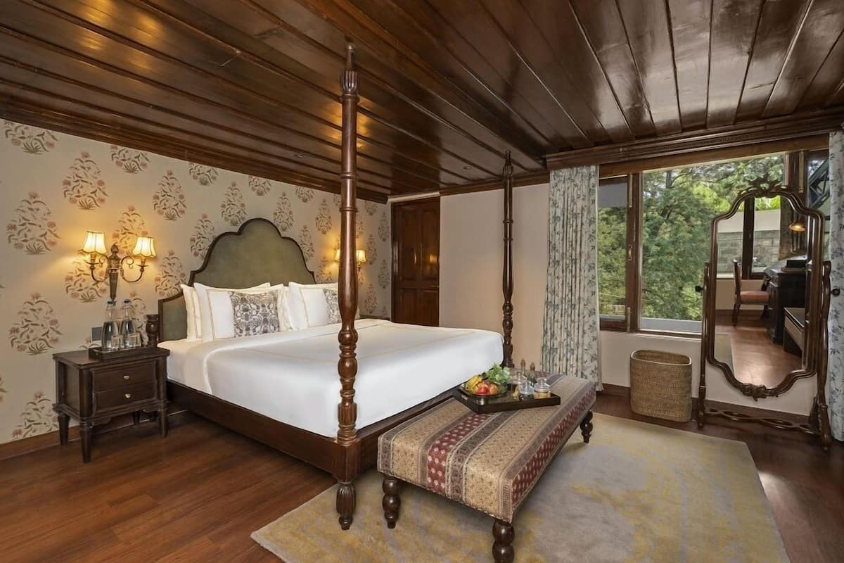 A four-poster bed with a wooden headboard, a bedside table with lamps, a bench, and a large mirror.