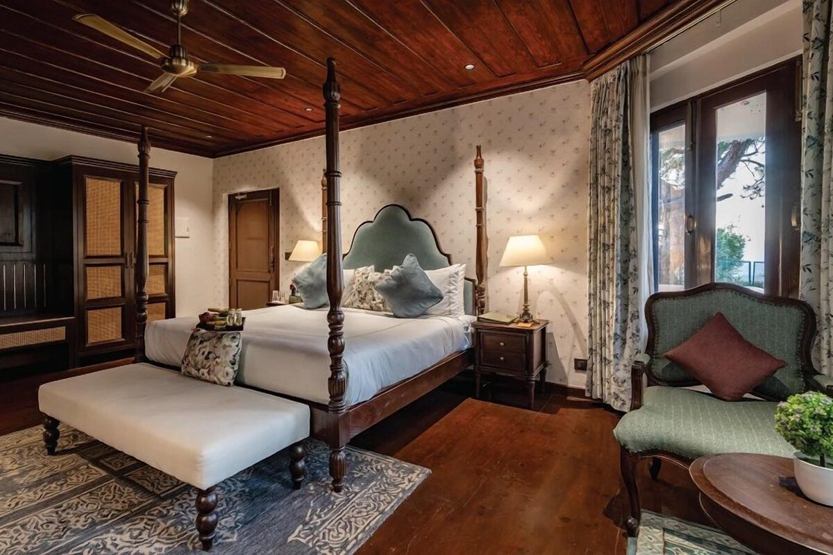 A four-poster bed with a canopy, a sofa, a chair, and a small table with a plant.