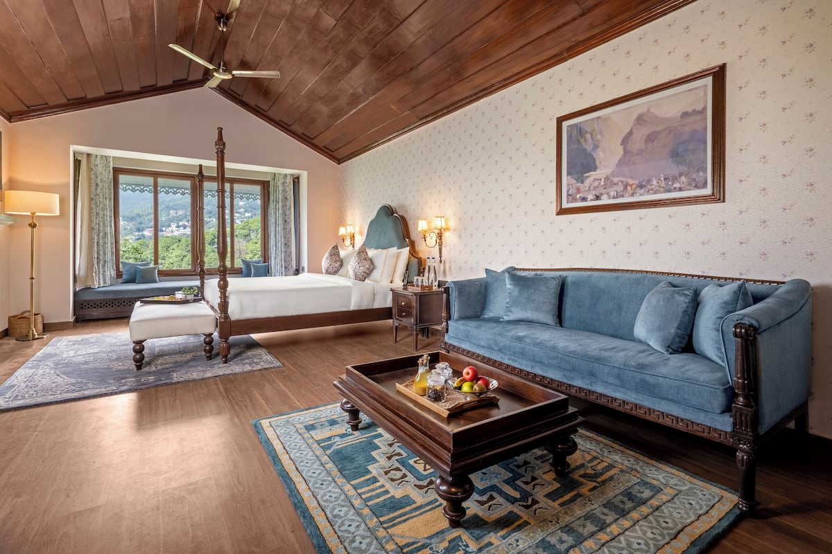 A spacious room with a large bed, a blue sofa, a wooden coffee table, and a view of the outdoors through a window.