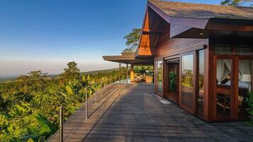 A modern wooden building with large glass windows, a wooden deck, and a view of lush greenery.