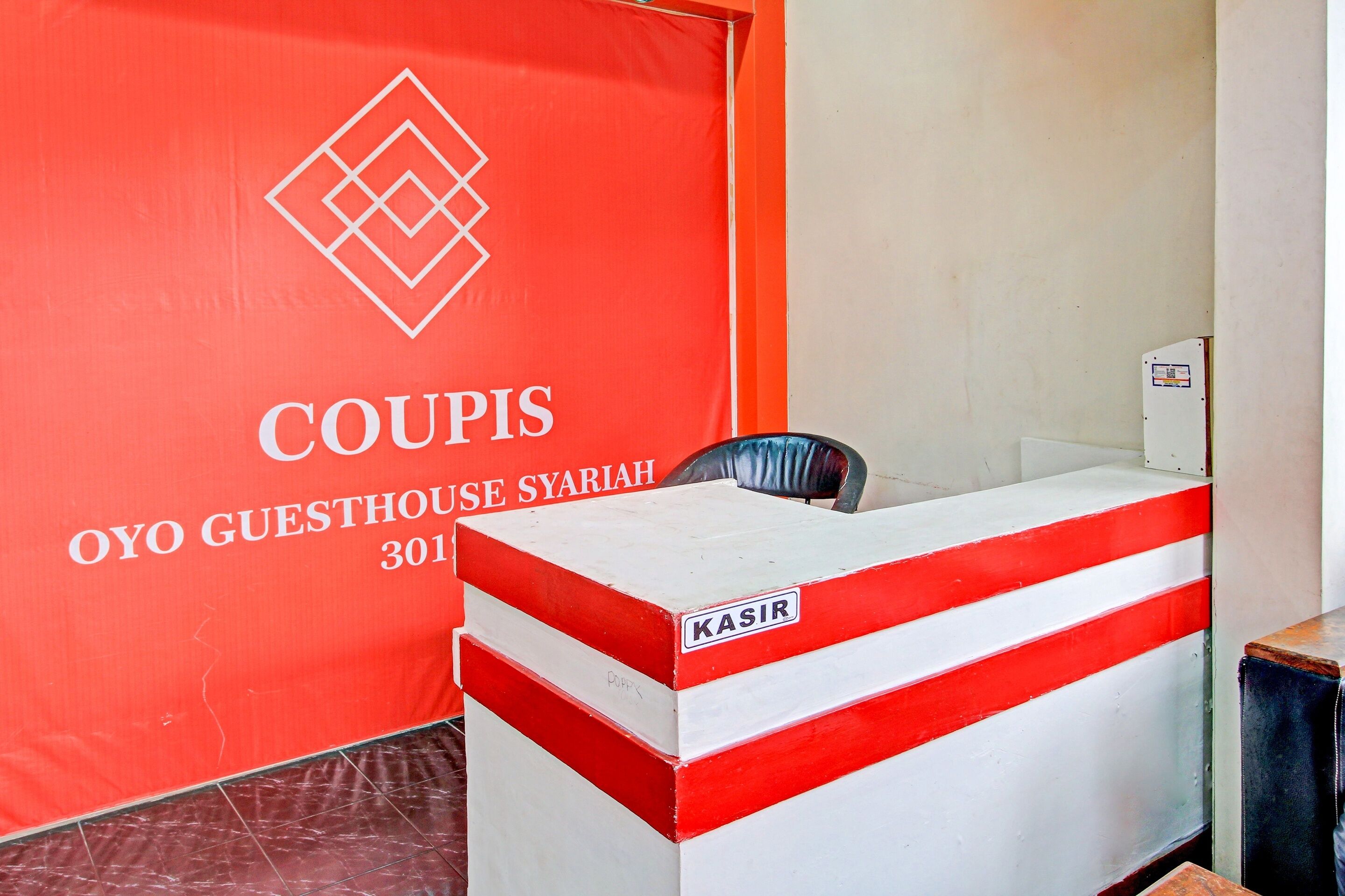 Una recepción con una decoración en rojo y blanco, un cartel que dice "COUPIS OYO GUESTHOUSE SYARIAH 301" y una etiqueta que dice "KASIR".