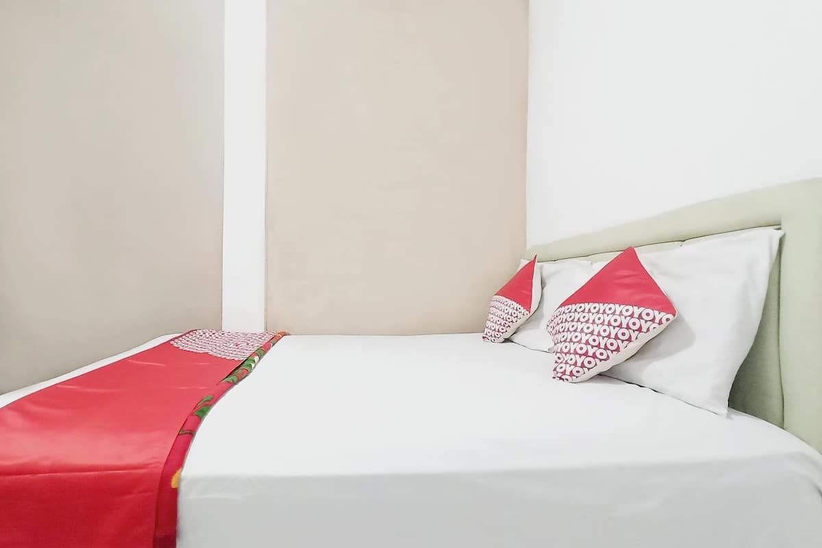 Una cama con ropa blanca y almohadas rojas, un tocador de madera y una pared lisa.