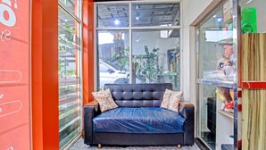 A room with a dark blue sofa bed, two pillows, a glass partition, and a view of the street outside. - OYO 3012 Coupis Guesthouse Syariah (Pare)