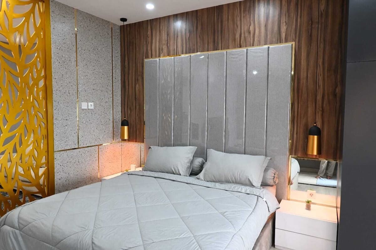 Ein modernes Schlafzimmer mit einem großen Bett, Holzvertäfelung und einem dekorativen, gelben Raumteiler.