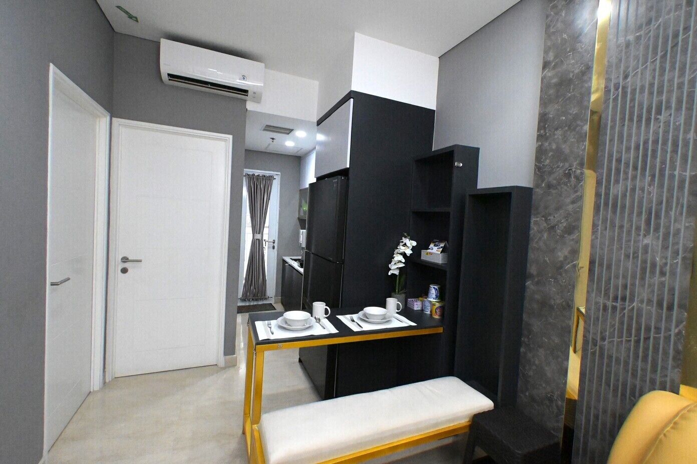 A compact hotel room with a kitchenette, a small dining table, a bench, and a wardrobe.