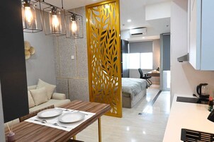 Una habitación de hotel moderna con zona de comedor, sofá, cama y un separador decorativo.