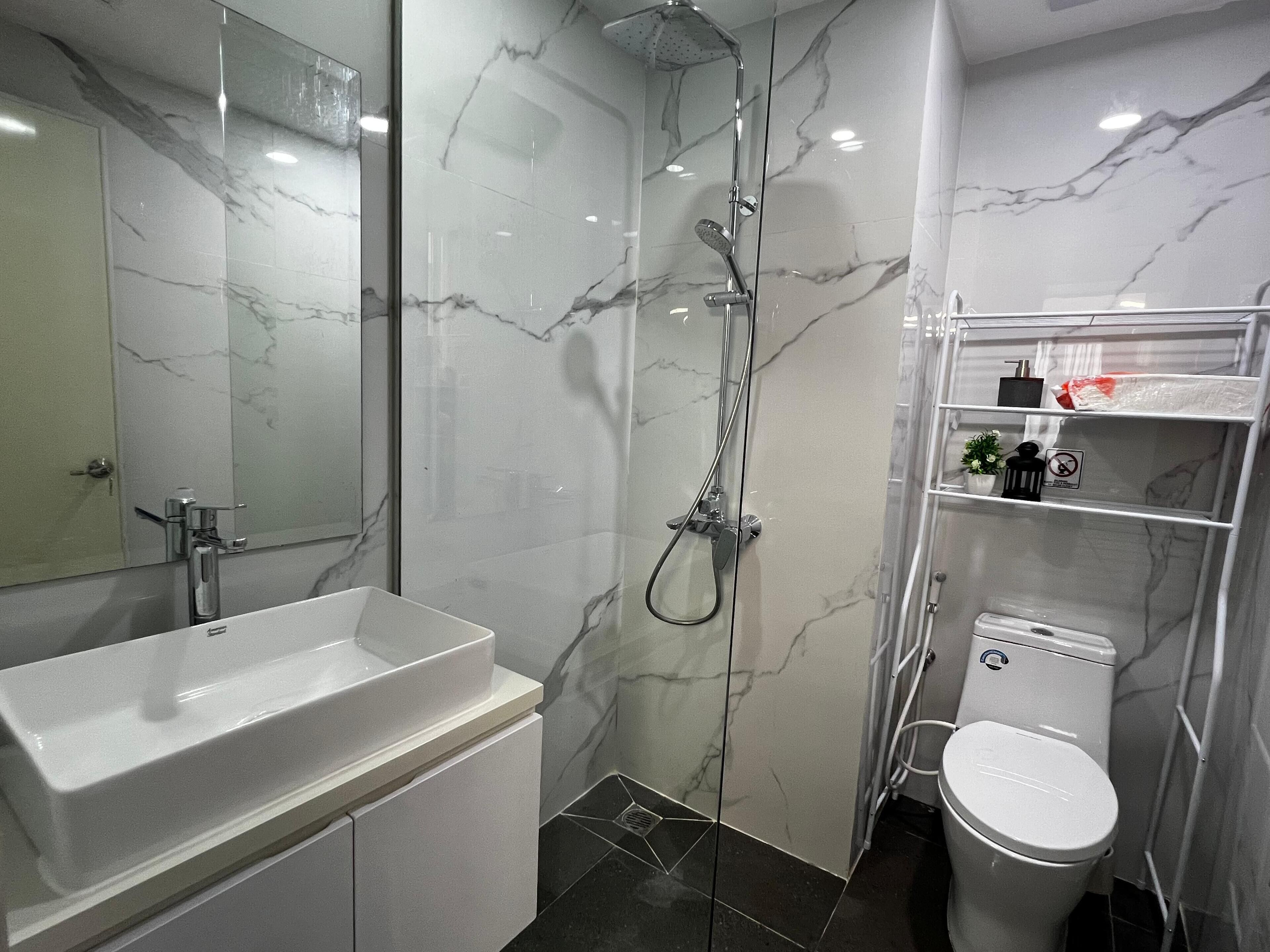 A modern bathroom with a marble shower, a white sink, and a toilet.