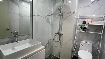 A modern bathroom with a marble shower, a white sink, and a toilet.
