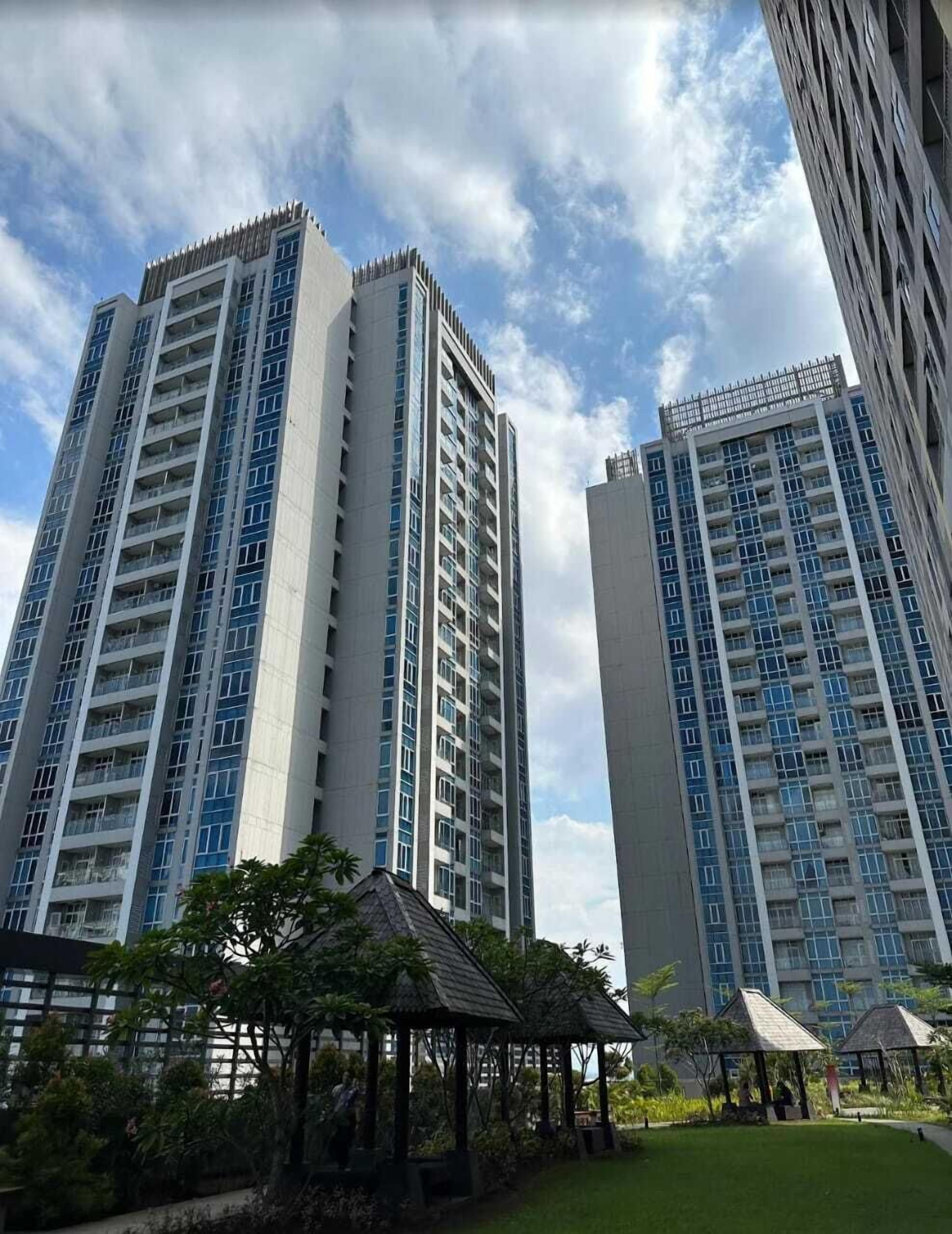 Two high-rise buildings with multiple floors, surrounded by a well-maintained garden with small structures.