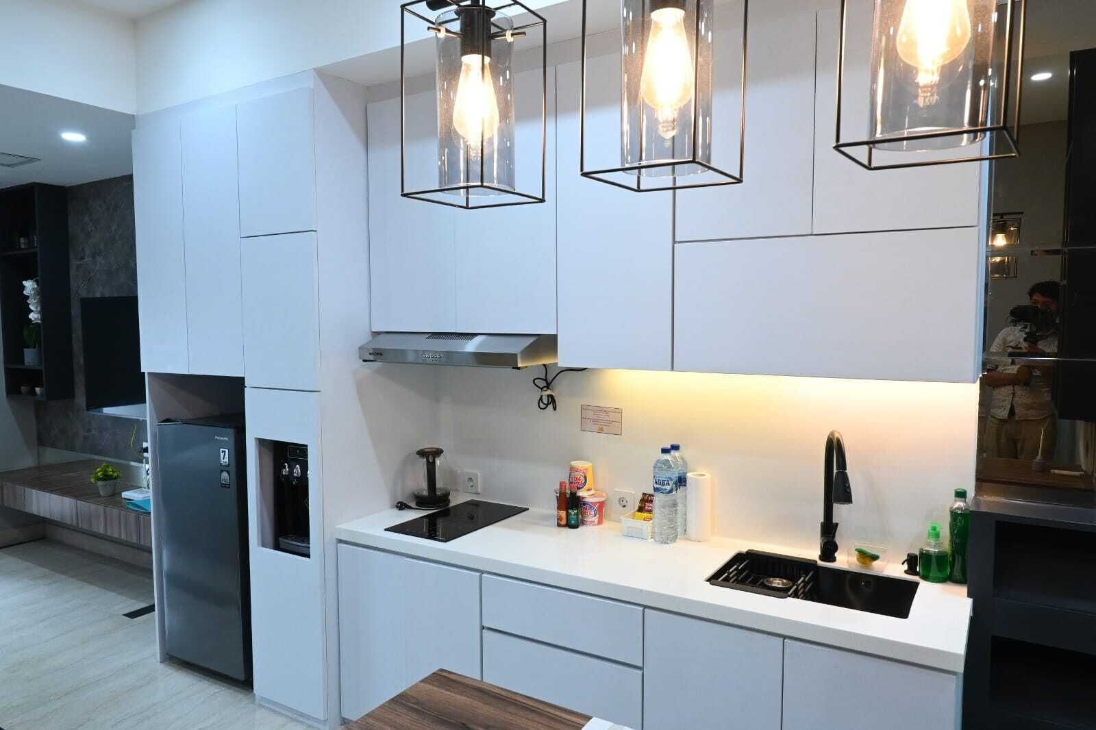 Eine moderne Küche mit weißen Schränken, einem Edelstahlkühlschrank, einem eingebauten Backofen, einem Gasherd und Pendelleuchten.
