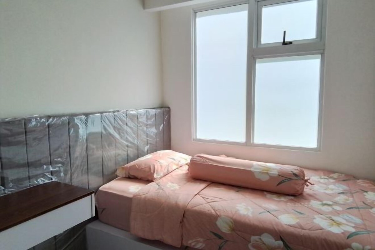 Un dormitorio con cama, mesita de noche y ventana.