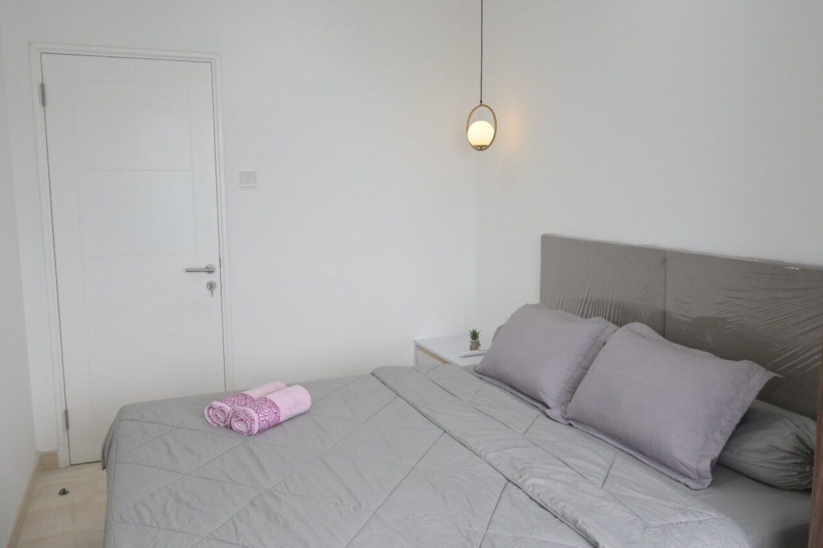 A bedroom with a bed, a nightstand, a lamp, and a door.