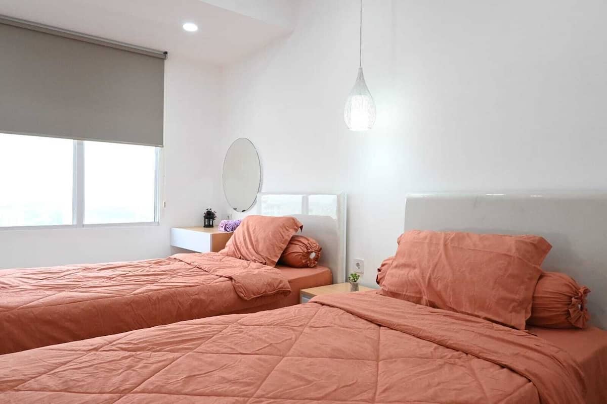 Ein modernes Schlafzimmer mit zwei Betten, einem Nachttisch, einem Spiegel und einer Hängeleuchte.