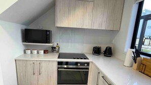 A compact kitchen with a microwave, toaster, and oven. - Coastal Sanctuary - Brand New Modern Townhouse (Christchurch)