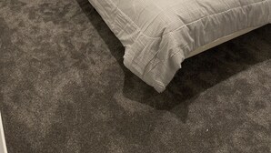 A neatly made bed with a grey bedspread, two white pillows, and a rolled grey blanket. There are two bedside tables with lamps and a wooden nightstand with a box. - Coastal Sanctuary - Brand New Modern Townhouse (Christchurch)
