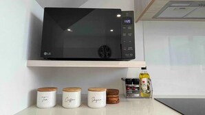 A kitchen with a black microwave on a white shelf, three labeled jars on the counter, and a spice rack with a bottle of olive oil. - Coastal Sanctuary - Brand New Modern Townhouse (Christchurch)