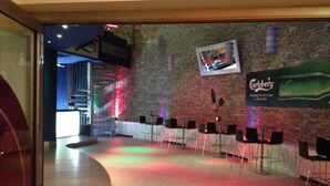A bar area with a brick wall, a mounted TV, and several tables and chairs. - Olimpic Village TH Sestriere apartments x6 (Sestriere)