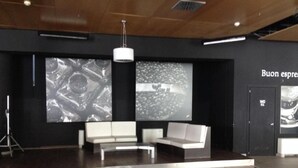 A modern lobby with a white sofa, a large screen displaying images, and a sign that reads "Buon espresso". - Olimpic Village TH Sestriere apartments x6 (Sestriere)