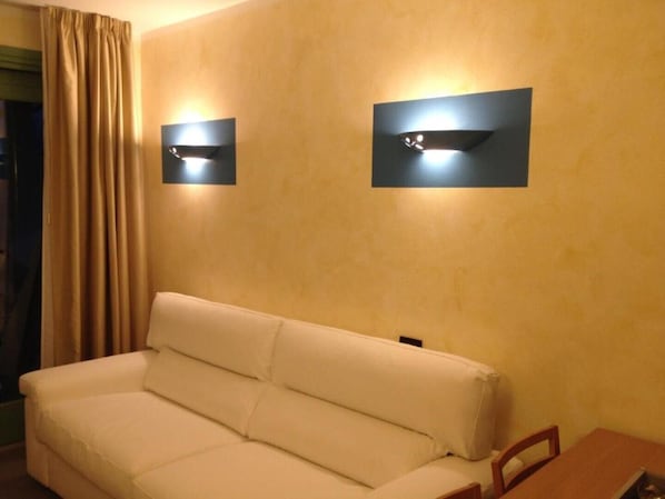 A room with a white sofa, two wall-mounted light fixtures, and a wooden table.