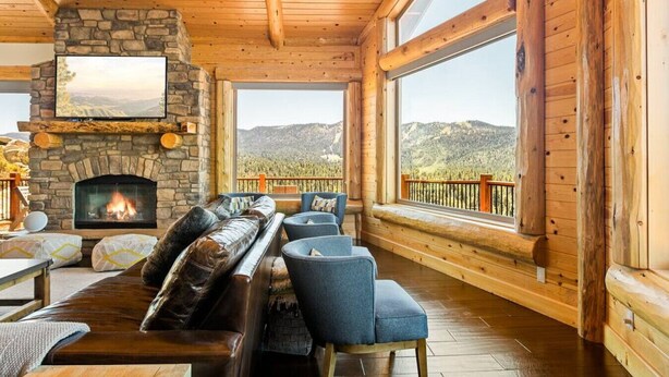 A cozy cabin interior with a stone fireplace, comfortable seating, and large windows offering mountain views.