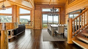 A wooden cabin interior with a dining area, a fireplace, and a view of the outdoors.