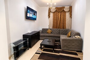 A modern living room with a flat-screen TV, a sofa, a coffee table, a cabinet, and a patterned rug. - Al Jazeerah Hotel (Sharjah)