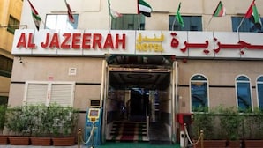 The entrance to Al Jazeera Hotel with a red sign, multiple flags, and a green carpeted area. - Al Jazeerah Hotel (Sharjah)