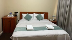 A hotel room with a bed, a wooden nightstand, a small cabinet, a telephone, and a window with curtains. - Al Jazeerah Hotel (Sharjah)