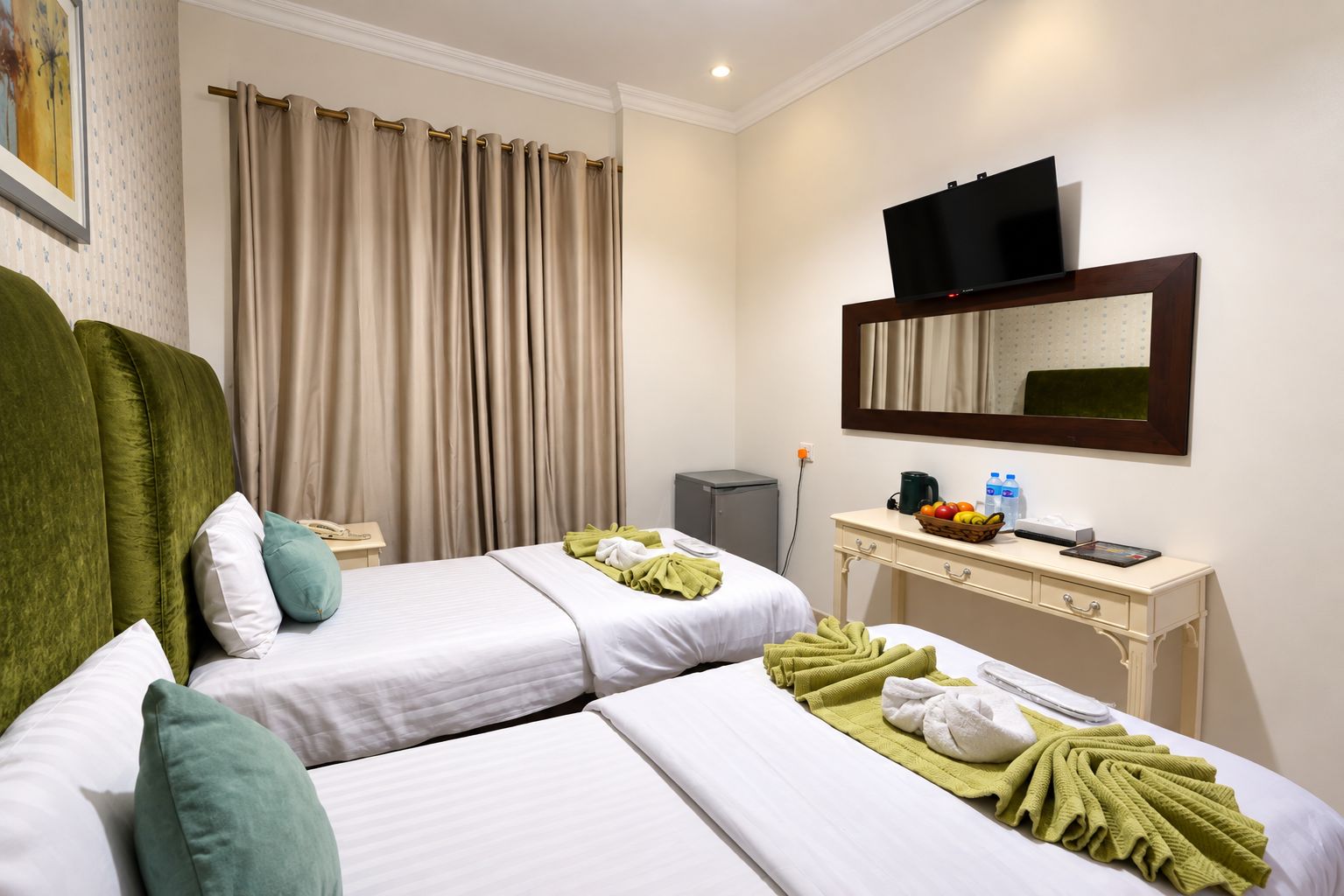 A hotel room with two beds, a desk with a television, and a mirror.