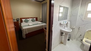 A hotel room with a bed, bedside table, lamp, and a bathroom with a sink, toilet, and shower. - Al Jazeerah Hotel (Sharjah)
