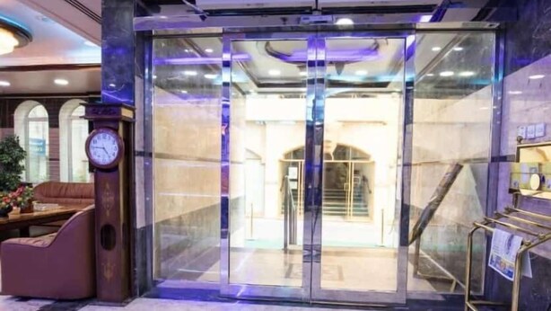 A hotel lobby with a marble floor, a clock, a reception desk, and a glass elevator. - Al Jazeerah Hotel (Sharjah)