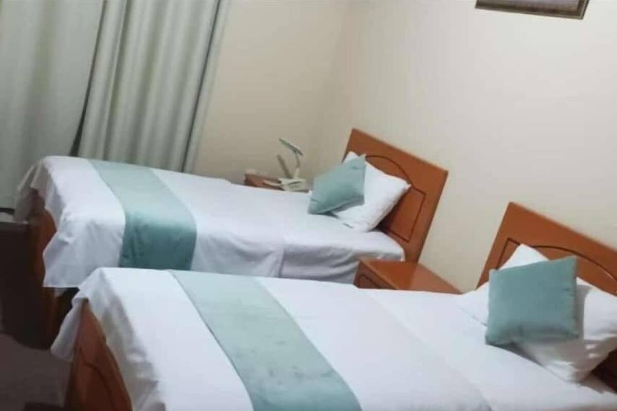 Une chambre d’hôtel avec deux lits simples, chacun doté d’une tête de lit en bois et de linge de lit blanc agrémenté de touches de couleur turquoise.