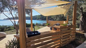 A wooden deck with a bench, a sink, and a shaded area overlooking a body of water. - Actaea, Relaxing Villa by the Seashore (Alonissos)