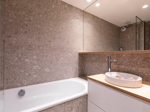 A modern bathroom with a freestanding bathtub, a round sink with a wooden countertop, and a large mirror above the sink.