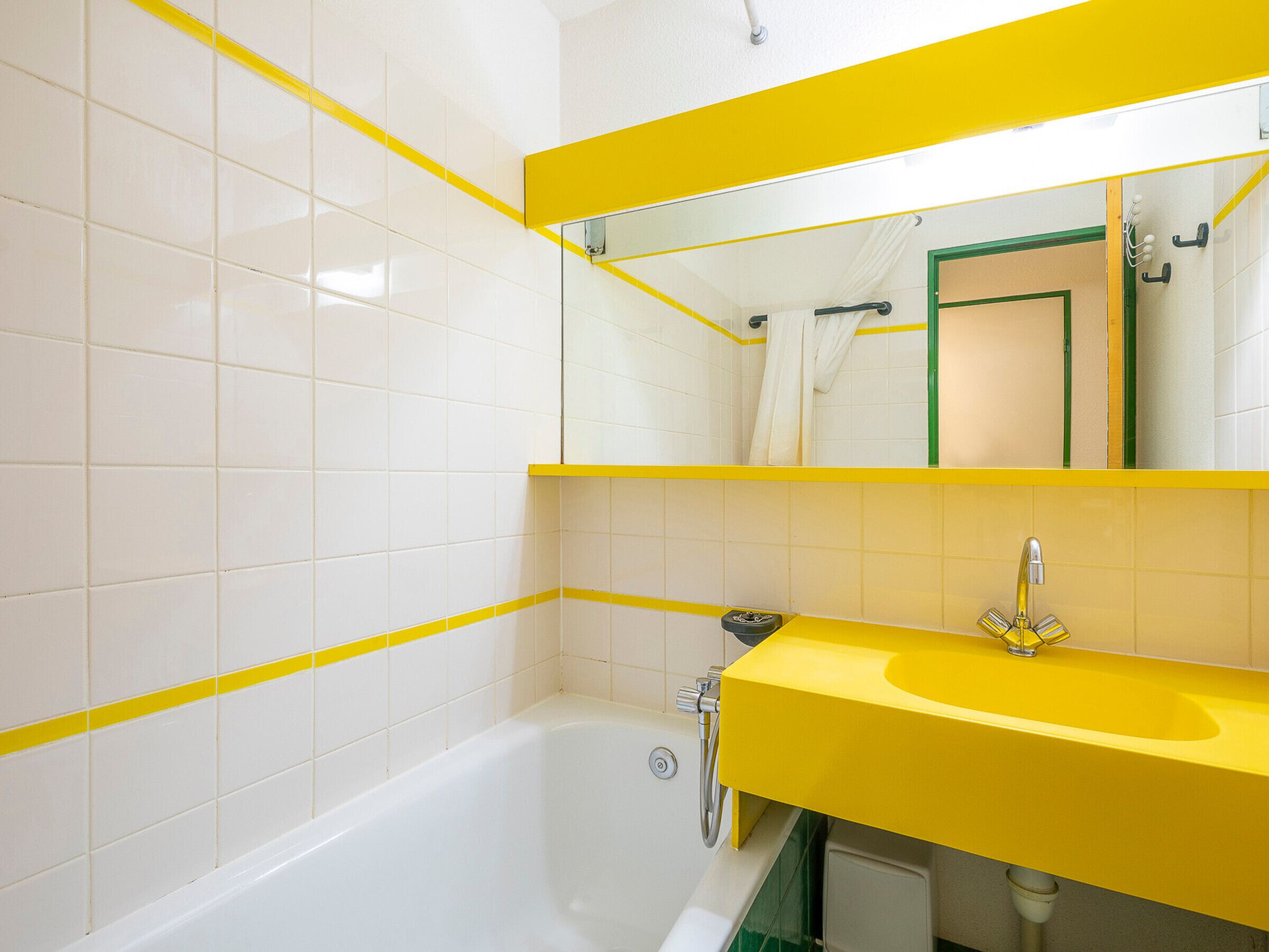 Une salle de bain avec des murs recouverts de carreaux blancs, un lavabo jaune et une baignoire.