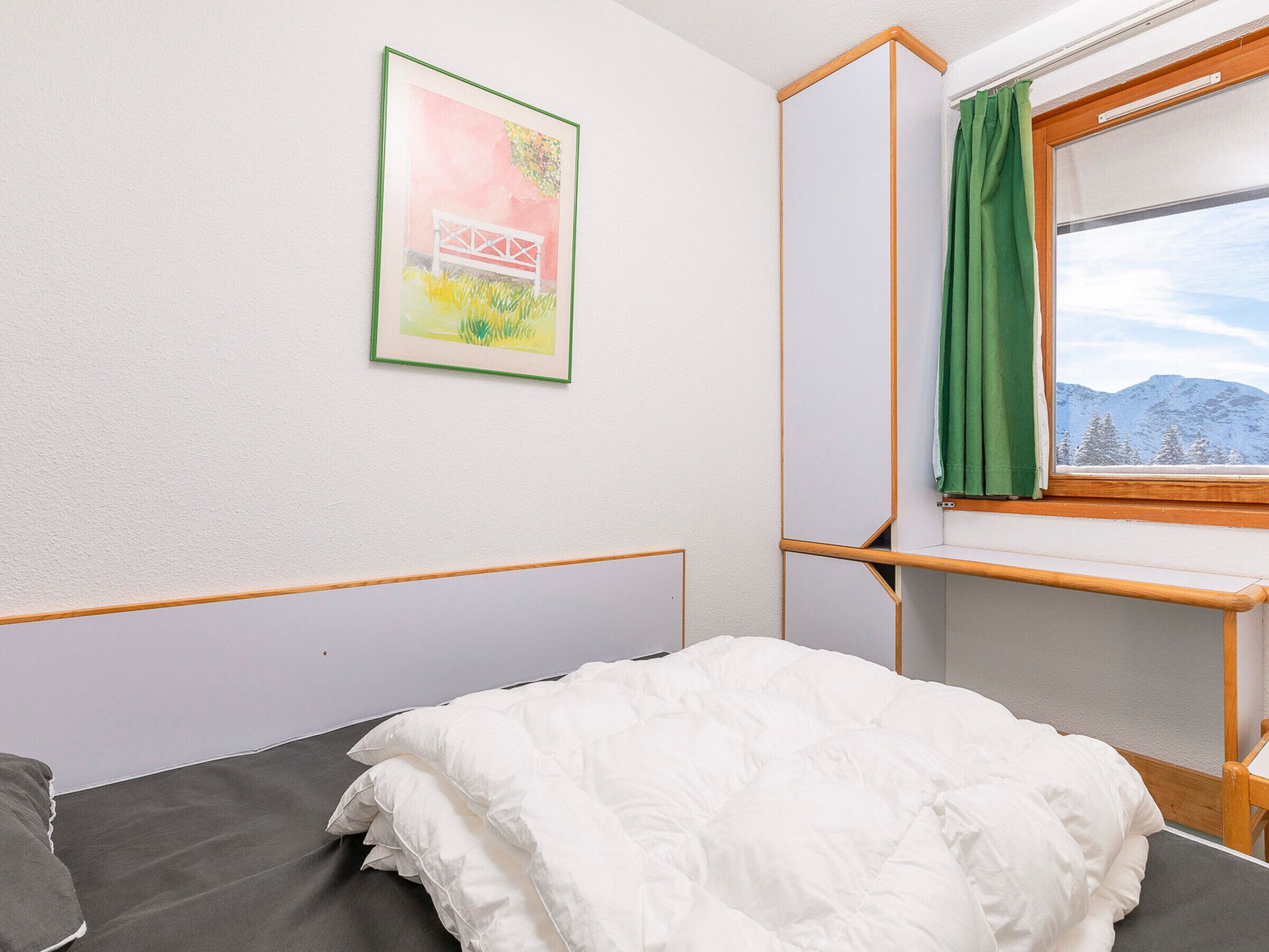 A bedroom with a bed, a window with a view of mountains, a green curtain, and a framed picture on the wall.