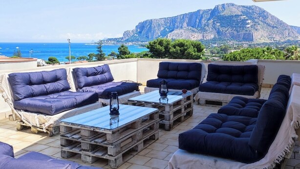 Une terrasse avec des sièges extérieurs, une vue sur la mer et une montagne en arrière-plan.