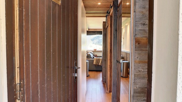 Un couloir intérieur en bois donnant sur un salon chaleureux et une fenêtre.