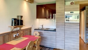 Une cuisine moderne avec une table et des chaises en bois, un four encastré et une fenêtre donnant sur un jardin.