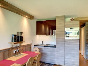 A modern kitchen with a wooden table and chairs, a built-in oven, and a window overlooking a garden.